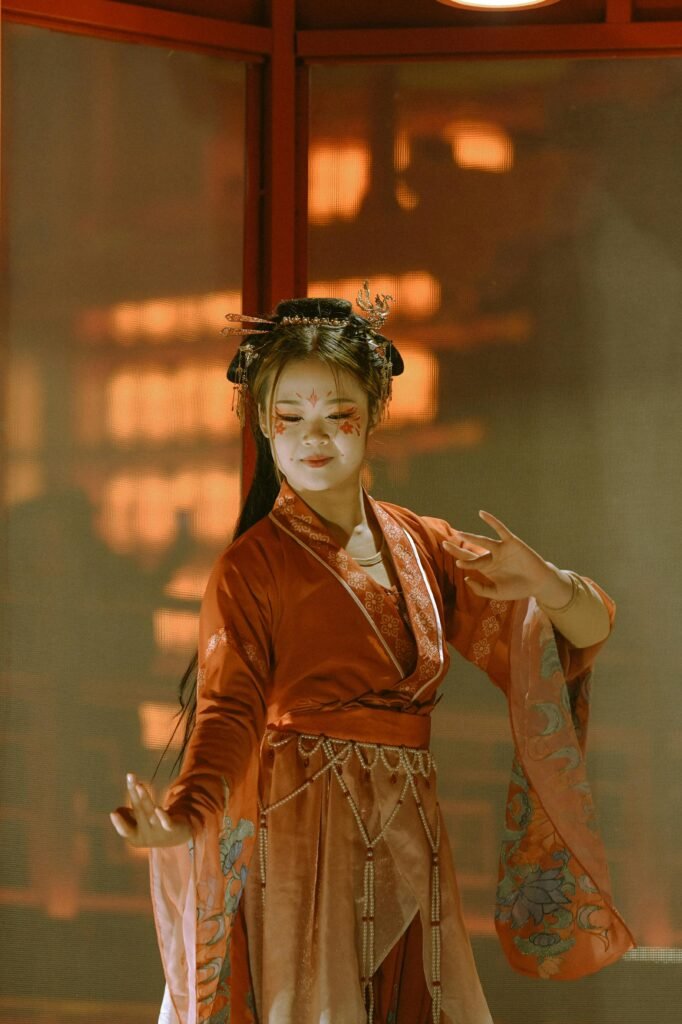 pexels-photo-15313370-15313370 Woman in red traditional Chinese dress with face paint, indoors setting.